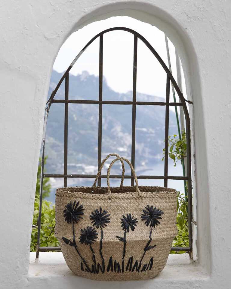 Borsa in paglia decorata con fiori neri, fotografia di moda con sfondo mare mediterraneo Costiera Amalfitana – Still life fashion by Bulb Studio